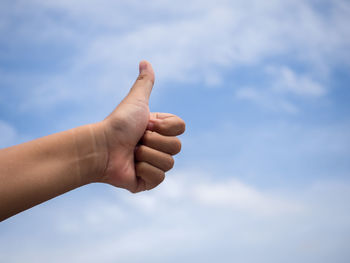 Cropped hand of person gesturing thumbs up against cloudy sky