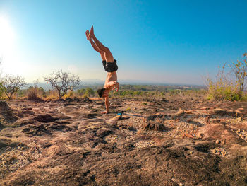 Full length of man doing hand standing on rocky surface against sky