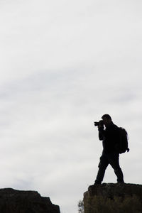 Man photographing on rock against sky
