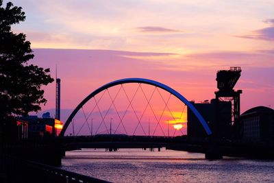Silhouette bridge over river against sky during sunset