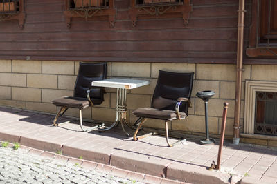 Empty chairs and table on sidewalk in city