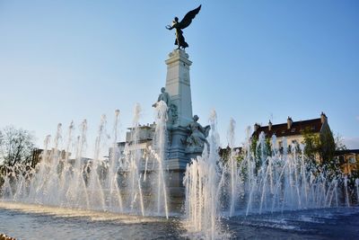 Low angle view of angel sculpture and fountain against clear blue sky