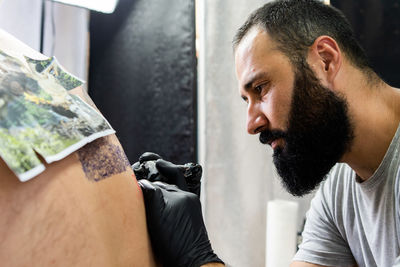 Close-up of artist tattooing customer in studio