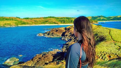 Woman standing on cliff by lake against blue sky