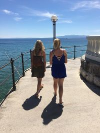 Rear view of women walking by railing against sea