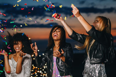 Cheerful friends with confetti enjoying at beach during sunset