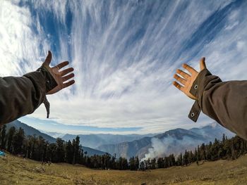 Cropped hands of person reaching cloudy sky