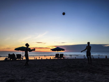 Silhouette people playing with ball at beach against sky during sunset