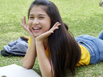 Portrait of smiling girl with book lying on field