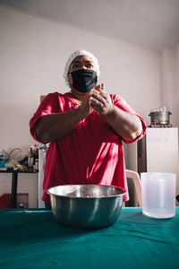 Venezuelan female in cloth face mask preparing arepas while looking forward at table with bowl at home