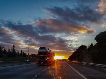 Cars on road against sky during sunset