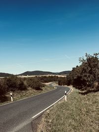 Road amidst trees against clear blue sky