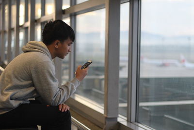 Side view of man using mobile phone at window