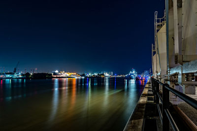 Illuminated city by sea against sky at night