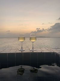 Wine glass on table by sea against sky during sunset