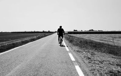 Rear view of man walking on road against clear sky