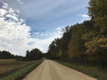 Empty road amidst trees on field against sky