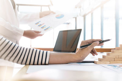 Cropped image of businesswoman holding pen while colleague showing graph at desk