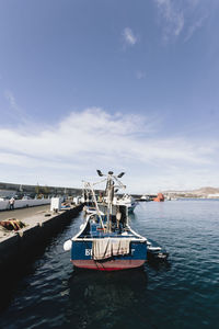 Fishing boat moored at harbor against sky