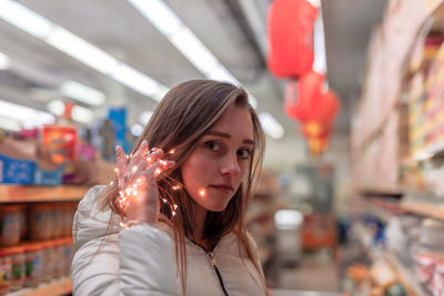 Portrait of young woman holding illuminated string light in supermarket