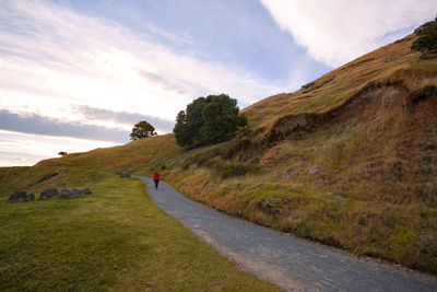 Woman walking on road by mountain against sky