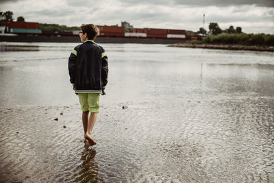 Young boy walk on vacation at mud flat shore and watch a passing container ship