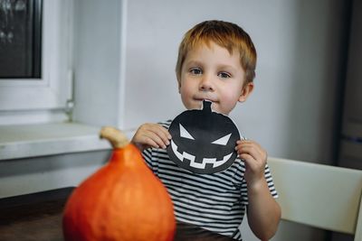 Little caucasian 3 year old boy holding paper pumpkin template to make a jack lantern out of pumpkin