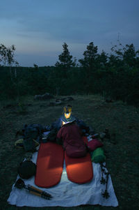 Woman sitting on field by trees against sky during winter