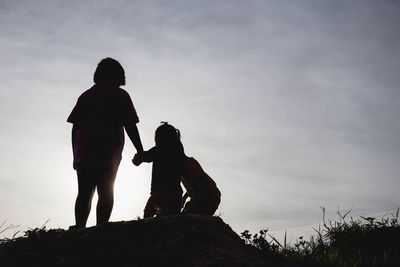 Rear view of silhouette women standing on rock against sky