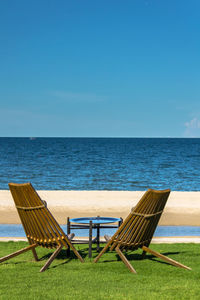 Empty chair on shore by sea against blue sky