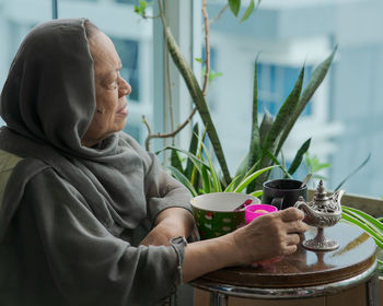 Senior malaysian muslim woman stay at home. sitting at the balcony apartment while having breakfast.