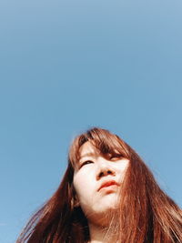 Low angle portrait of young woman against sky