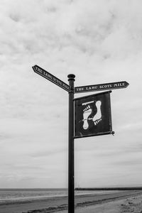 Information sign by sea against sky