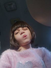 Low angle portrait of girl sticking out tongue against ceiling