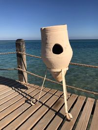 Wooden railing on pier by sea against clear blue sky