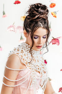 An attractive young woman in a pink short dress in a light spring studio with floating flowers. 