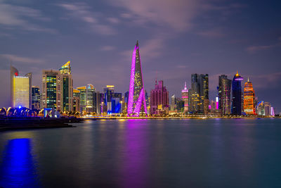 Illuminated buildings by river against sky at night