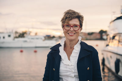 Portrait of smiling senior woman at harbor during sunset