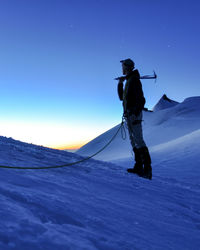 Low angle view of man with climbing equipment standing on snow covered land against sky at dusk