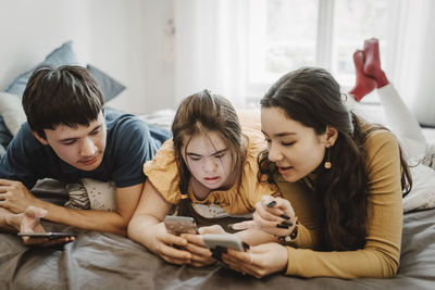 Curious male and female siblings sharing smart phone while lying down on bed at home