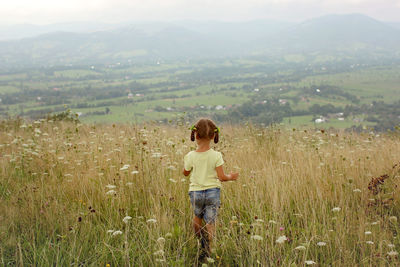 Adorable preschooler girl walking happily in wheat and flower field among mountains