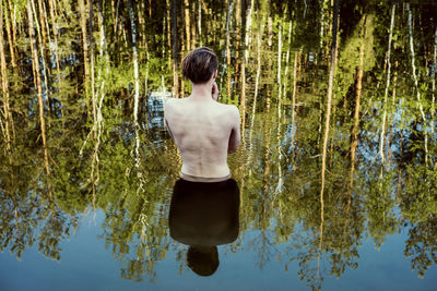 Rear view of shirtless mid adult man standing in lake at forest