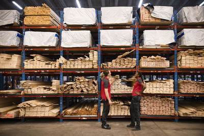 Side view of male and female sales staff talking to each other near rack at hardware store