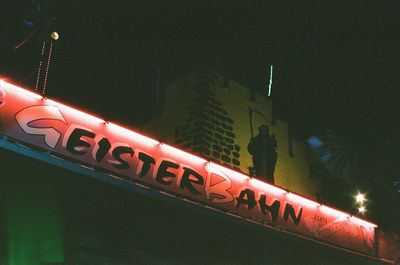 Low angle view of illuminated text on building against sky at night