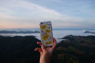 Close-up of hand holding smart phone with text against sky