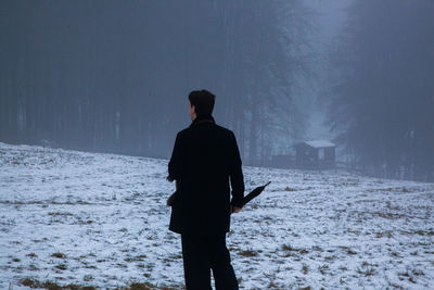 Rear view of silhouette man standing on snow covered land