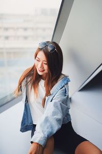 High angle view of smiling woman sitting by window on tiled floor