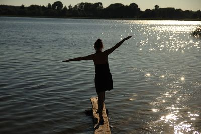 Full length of woman with arms outstretched walking on wood over lake during sunset