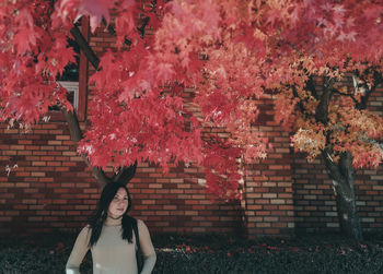 Portrait of young woman standing by pink flowering tree