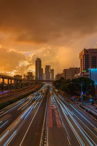 High angle view of light trails on highway in city against sky during sunset